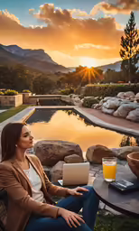 a woman sits at an outdoor table, with a laptop and orange juice in her lap