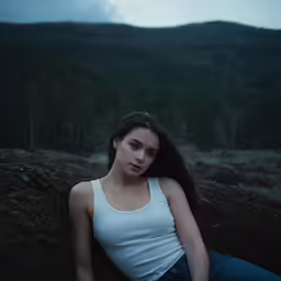 a girl is sitting in the dirt with mountains behind her