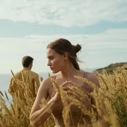 a woman in a dress standing in the tall grass near a man