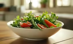 a salad with greens and tomatoes on top of a wooden table