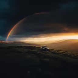the car is driving down the dirt road in front of a rainbow