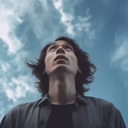 an image of a man that is looking up in the air,a man looking up into the sky with a cloud background