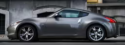 the shiny silver nissan sports car is on the street,a shiny silver car parked by the curb