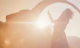 a woman standing near some rocks and looking at the sun