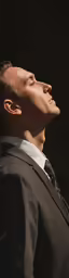 a male in a black jacket with a white shirt and tie