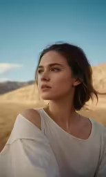 a young girl wearing a white top standing in a desert