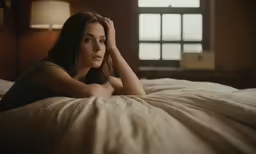 a beautiful woman laying on top of a bed next to an open window