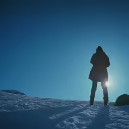 person standing on snow in front of the sun
