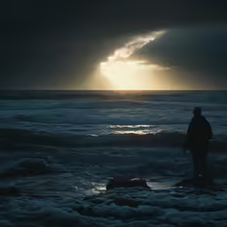 the person is standing in the water watching the sun set