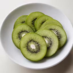 sliced kiwi in a white bowl sitting on top of a table