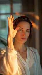 a woman poses for a portrait with her hand up to the side,a young woman touching her hand while sitting in front of a window