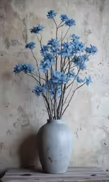 small white vase with blue flowers sitting on a shelf