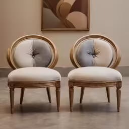 the back of two chairs with circular legs in front of a painting