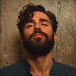 a man wearing a blue shirt stares up with a dark brown beard