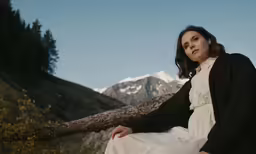 a woman in a dress is sitting on a log