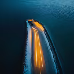 two long lines of light streak across a snowy road near a body of water