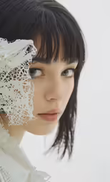 a young woman is holding a lace piece over her face