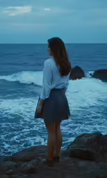 a woman looks out at the ocean while standing on a rock