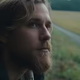 a man with a long hair and beard wearing an apron looks out over a field