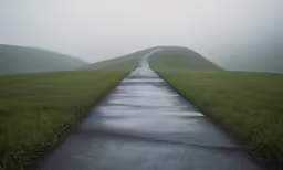 a long empty road is near grassy hills