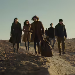 group of people in brown trenchs walking up sand covered hillside