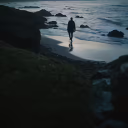 person walking on beach near the ocean on a cloudy day