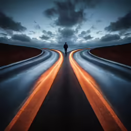 the silhouette of a person standing on an asphalt road at night