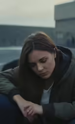 a young girl in green jacket sitting on ground looking down