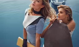 two women standing next to each other with boats in the background