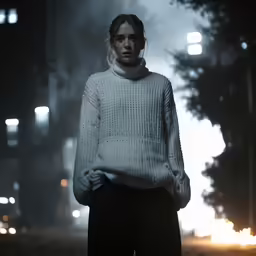 a model wears a grey knit sweater as a dark evening walks behind her