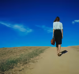 a woman walking up a dirt road in a dress