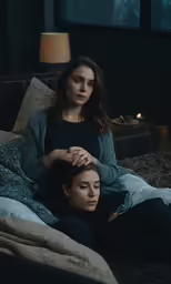 a woman sitting on a bed next to another girl