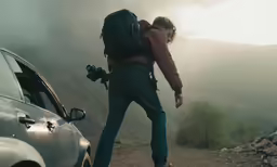 man looking at car in the mountains with backpack on back