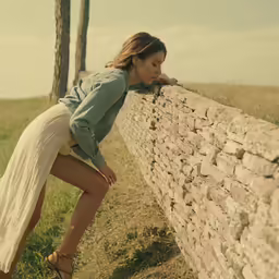 young woman leaning on stone wall while posing