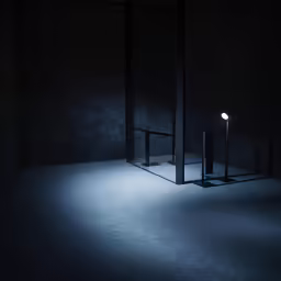 an illuminated lamp sits on a floor in a dark room