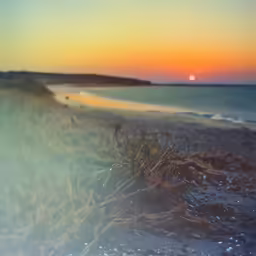 the sun is setting on the horizon over the beach