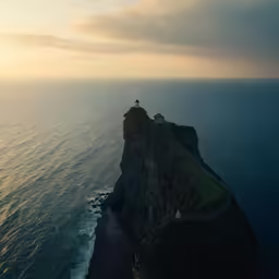 a very high hill side with an ocean and a light house on top of it
