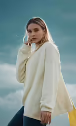 a blonde woman in a cream colored sweater, blue jeans and brown shoes