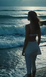 a young lady standing on the beach looking at the water