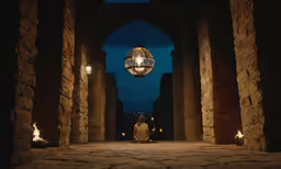 man sitting underneath a bright light surrounded by pillars