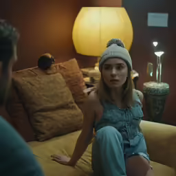 a woman wearing a hat is sitting on a couch in a dimly lit room