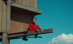 a woman in red standing by a wooden structure