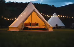 a bed and chair in a teepee set up in a grassy field
