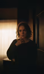 a woman poses with her arms crossed in front of the window