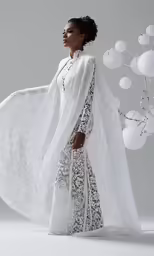 a woman in white wearing a long dress with a white cape and black floral lace on the front