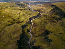 a valley with a stream of water running between it and some hills in the background,an aerial view of green landscape from an airplane