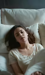 a woman laying in bed sleeping with the blanket blowing in