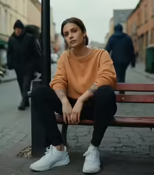 a woman in a tan sweater sits on a wooden bench