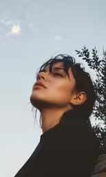 a woman stares up at the sky next to trees