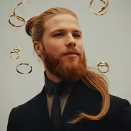 man with a beard wearing a suit and gold rings in his hair